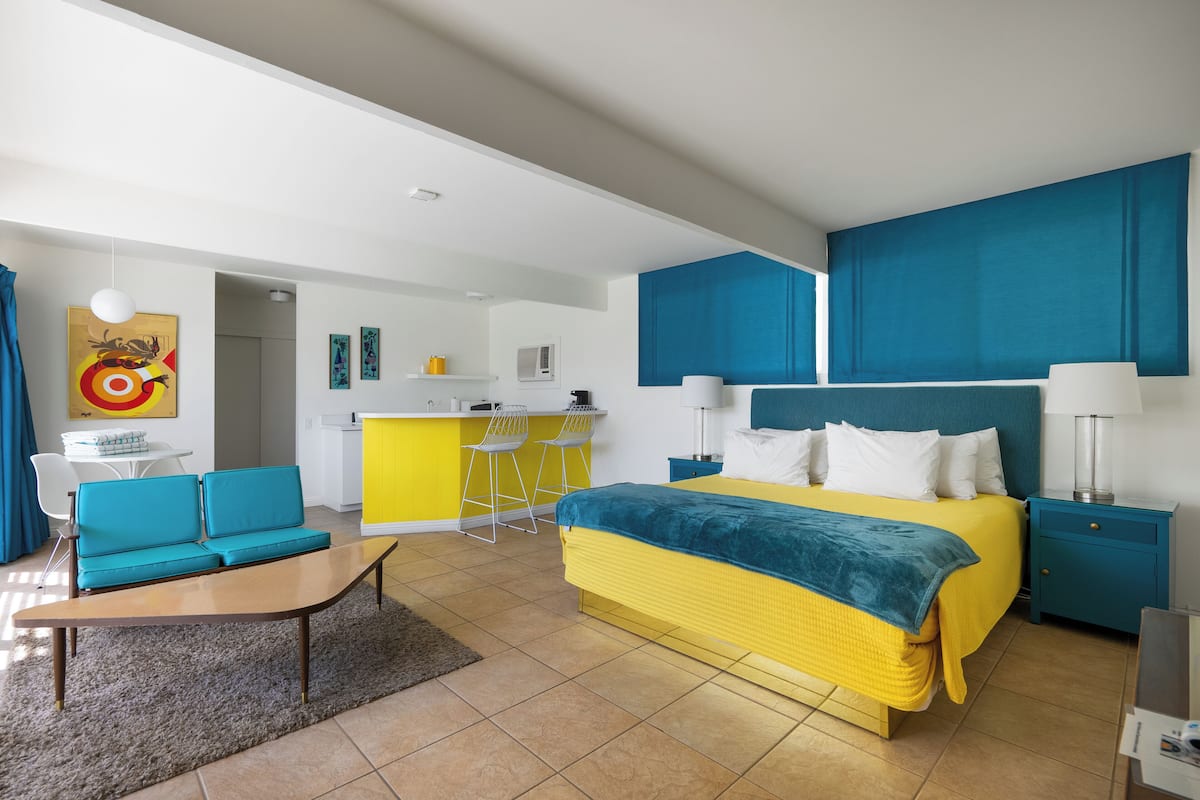 Ein modernes Hotelzimmer mit Bett, einer Sitzecke, einem Schreibtisch und einer Küchenzeile.