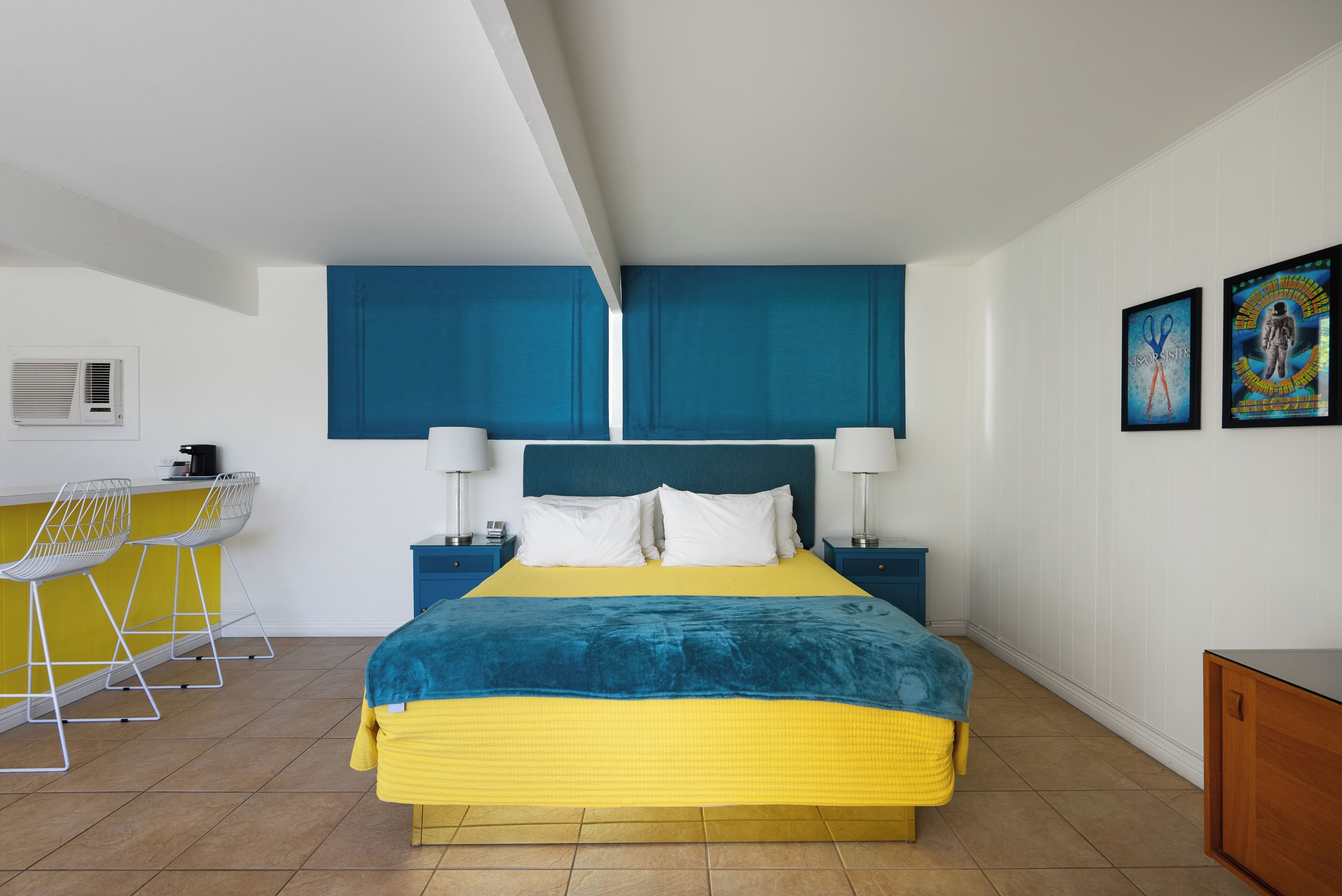 Une chambre à coucher comprenant un lit, des tables de chevet, un bureau avec des chaises et un climatiseur fixé au mur.
