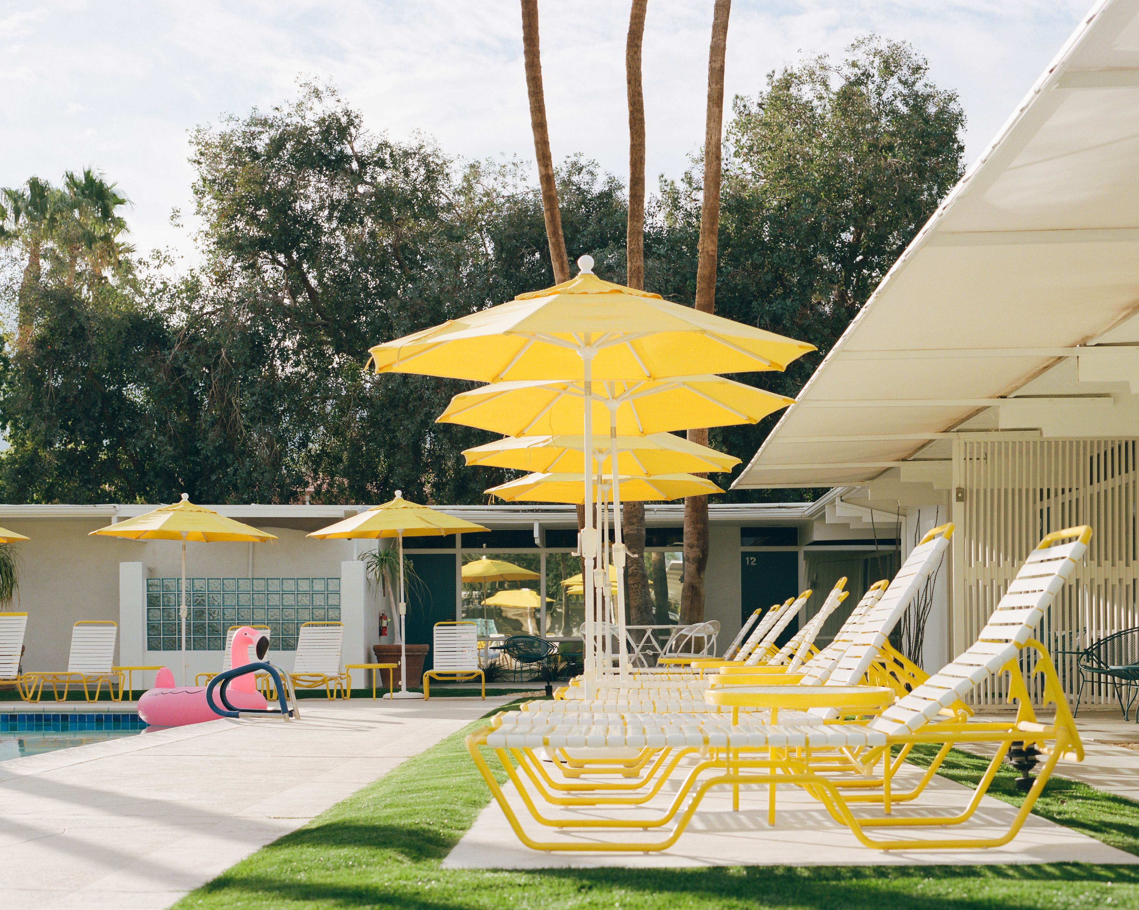 A pool area with yellow umbrellas, white lounge chairs, and a pink flamingo float.