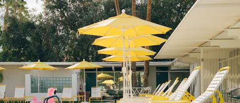 A pool area with yellow umbrellas, white lounge chairs, and a pink flamingo float.