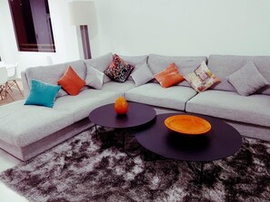 A modern living room with a grey sofa, multiple colorful cushions, two black coffee tables, and a shaggy rug.