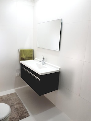 A modern bathroom with a white sink, black cabinet, and a mirror above it. - Oxygène (Marrakech)