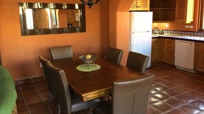 A dining area with a wooden table and chairs, a decorative centerpiece, and a kitchen in the background.