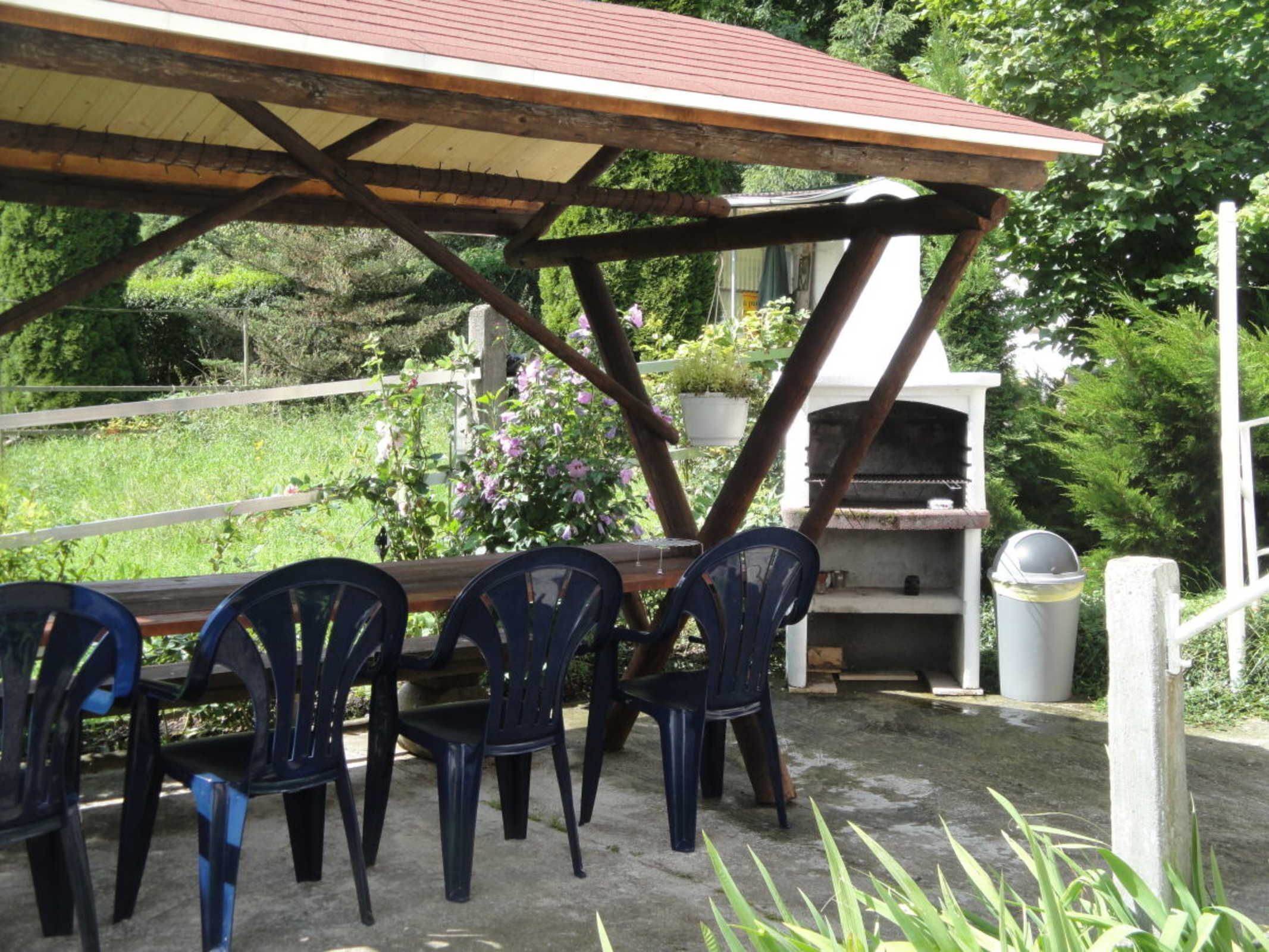 An outdoor patio with a wooden table and chairs, a barbecue grill, and potted plants.