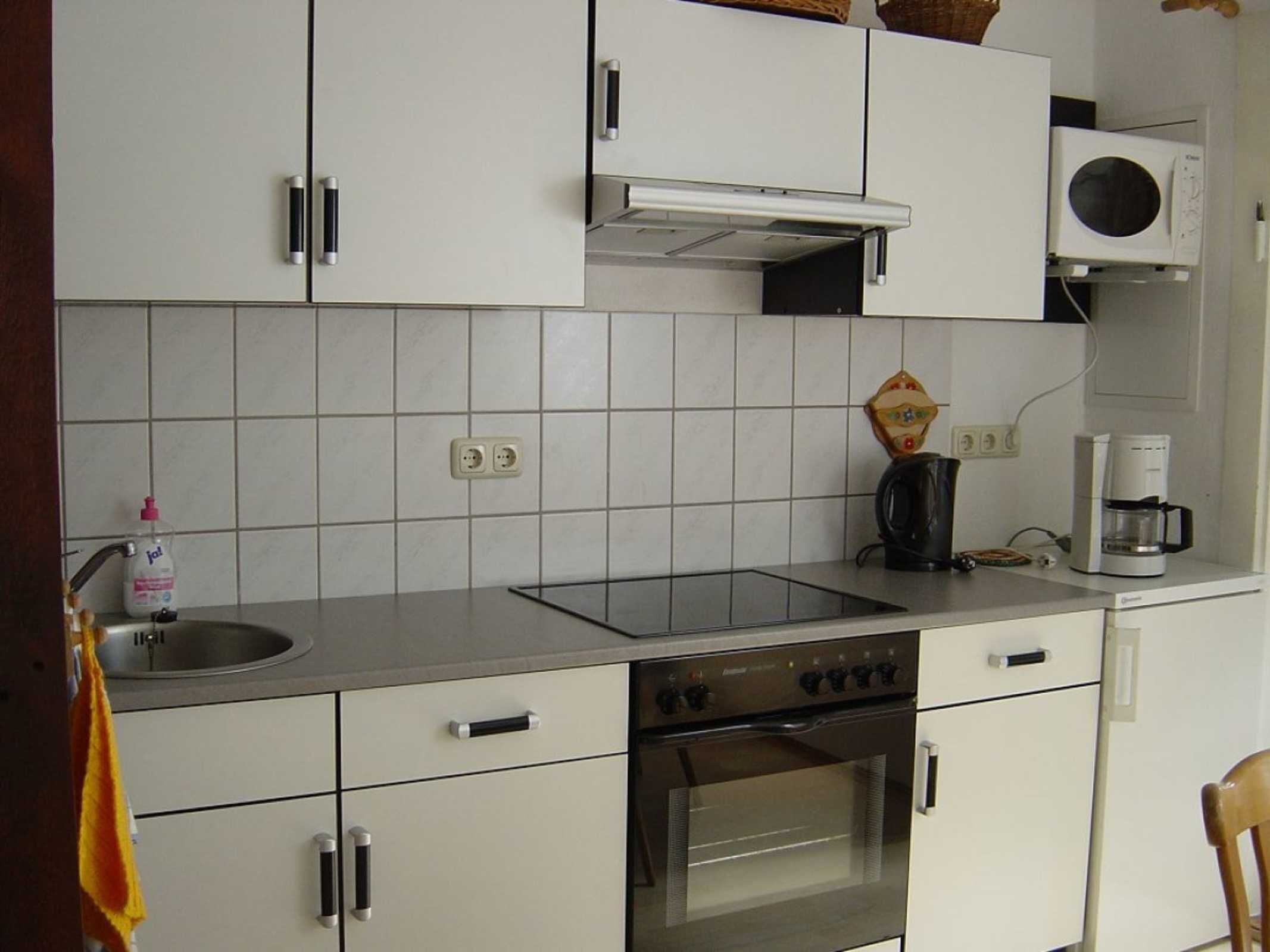 A compact kitchen with white cabinets, a built-in oven, a microwave, and a coffee maker.