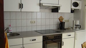 Una cocina compacta con armarios blancos, horno integrado, microondas y cafetera.