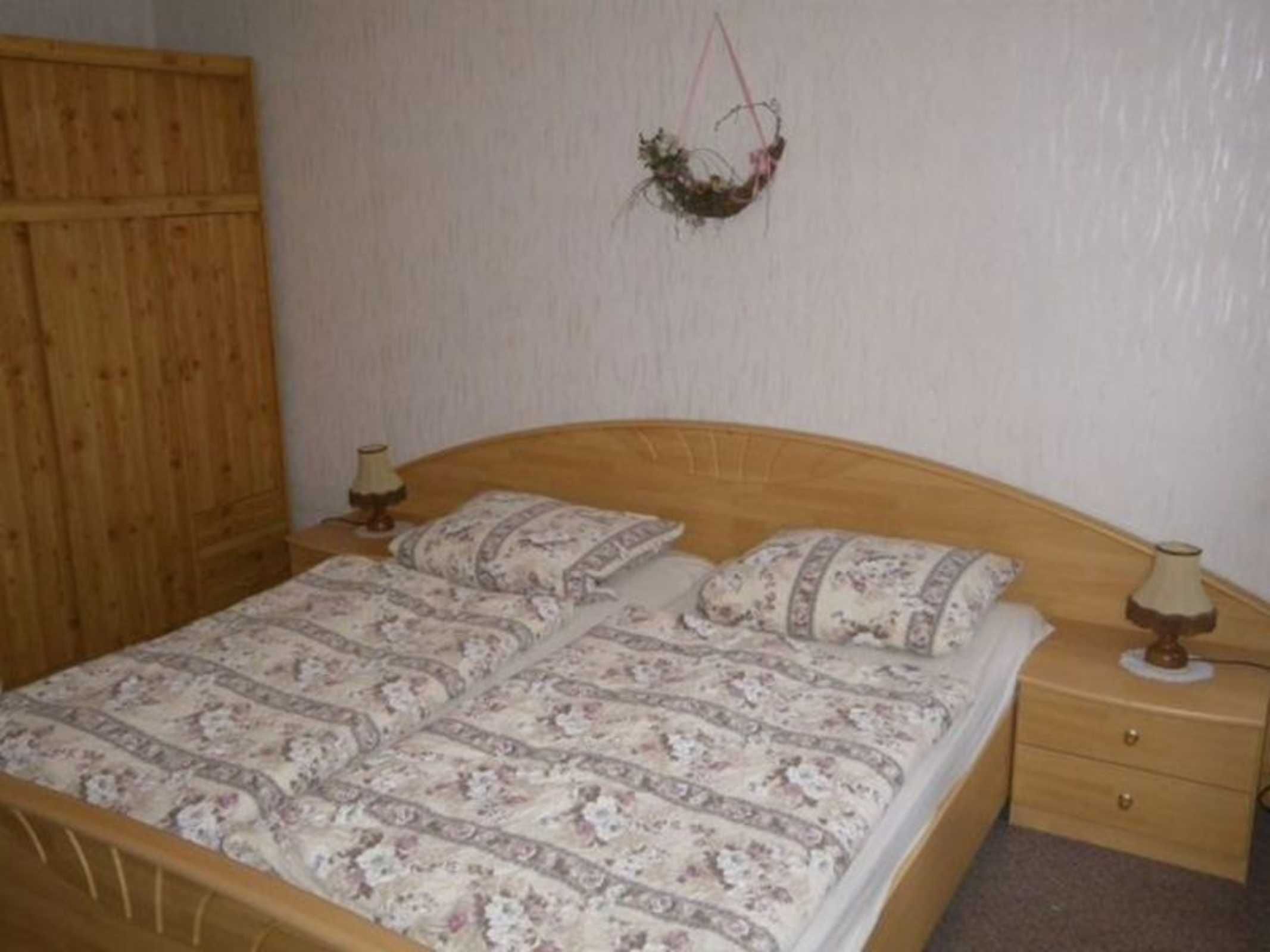 Un dormitorio con una cama de madera, ropa de cama floral, una mesita de noche y una planta colgante.