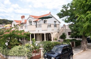 A two-story house with a red-tiled roof, a balcony, and a parked car.
