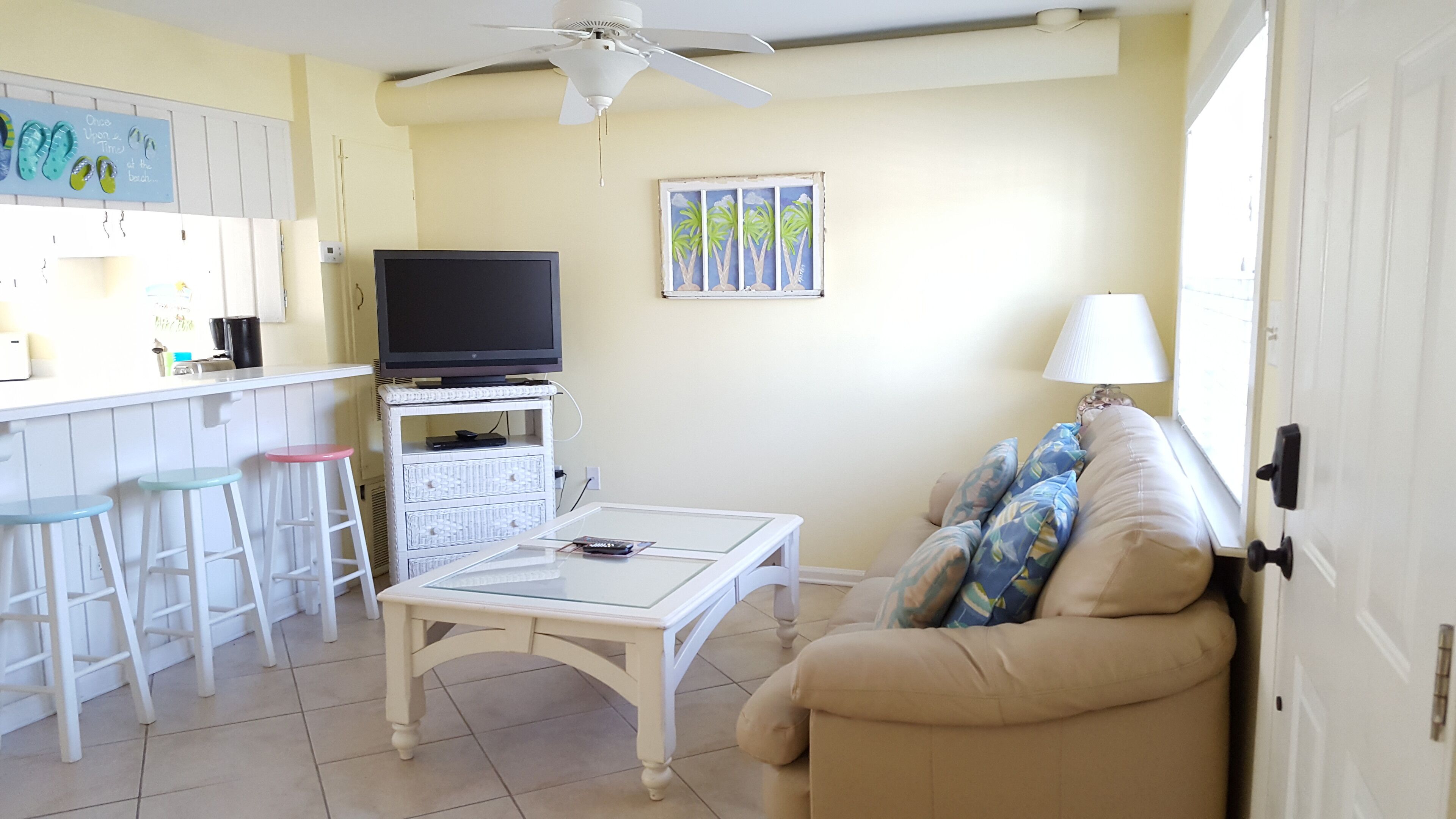 Una sala de estar con televisor, una mesa blanca, un sofá color beige y un ventilador de techo.