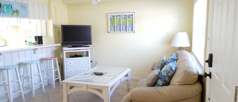 Una sala de estar con televisor, una mesa blanca, un sofá color beige y un ventilador de techo.