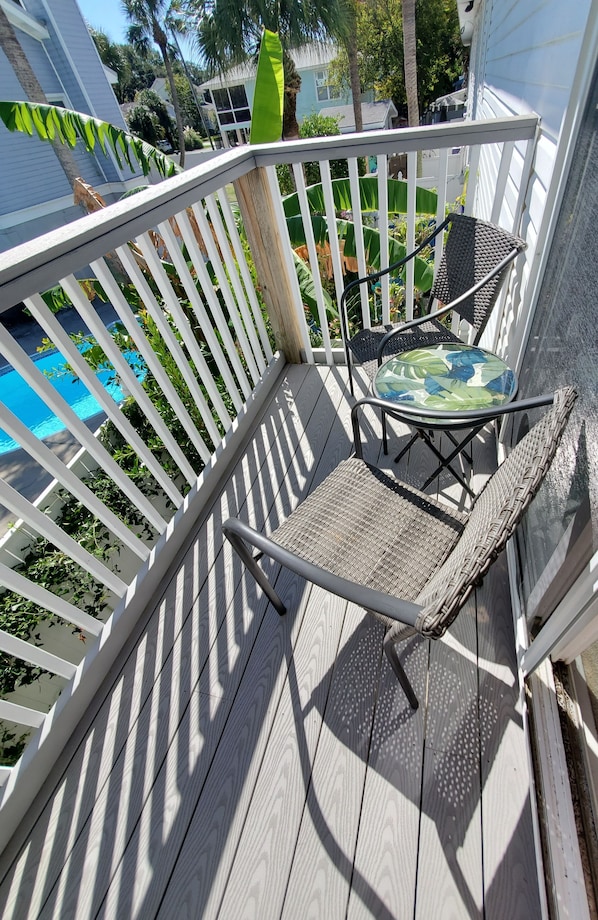 A wooden deck with a white railing, a wicker chair, and a small table with a green and blue patterned tablecloth.