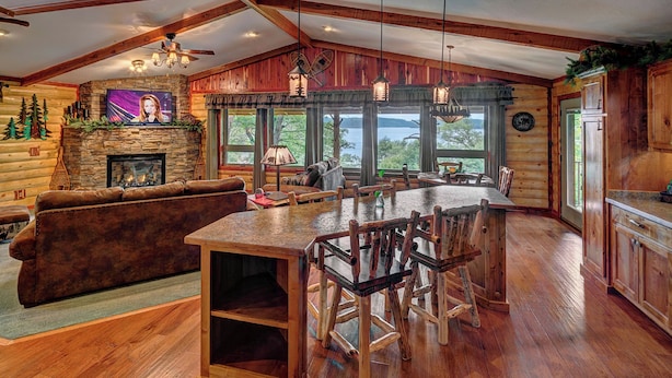 A rustic cabin interior with a stone fireplace, wooden dining table, and a cozy seating area.