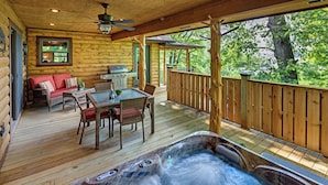 A wooden deck with a hot tub, outdoor furniture, and a view of trees.