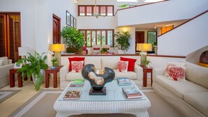 A spacious living room with a high ceiling, a central coffee table, and a staircase leading to an upper level. - Punta Aguila Spectacular 4 Bdr / 6 Bath Free Golf Cart  Chef and Waiter Included (La Romana)