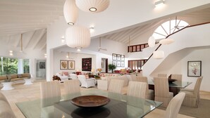 A spacious living area with a glass dining table, comfortable seating, and a staircase with a unique design. - Punta Aguila Spectacular 4 Bdr / 6 Bath Free Golf Cart  Chef and Waiter Included (La Romana)