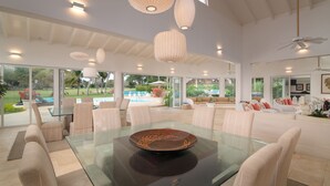 A spacious living area with a glass coffee table, comfortable seating, and large windows offering a view of a pool and garden. - Punta Aguila Spectacular 4 Bdr / 6 Bath Free Golf Cart  Chef and Waiter Included (La Romana)