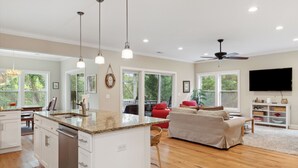 A spacious living area with a kitchen island, wooden flooring, and a ceiling fan. - Ample outdoor living spaces, Short walk to beach, Get a little "Sand In Your Shoes' (Folly Beach)