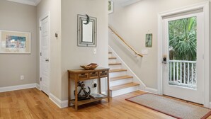 A hallway with wooden flooring, a white door, a staircase, and a small console table with a basket and a mirror. - Ample outdoor living spaces, Short walk to beach, Get a little "Sand In Your Shoes' (Folly Beach)