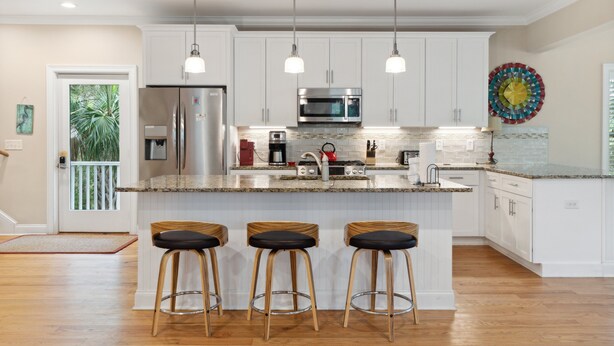 A modern kitchen with white cabinets, stainless steel appliances, and a central island with bar stools. - Ample outdoor living spaces, Short walk to beach, Get a little "Sand In Your Shoes' (Folly Beach)