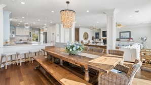 A spacious dining area with a wooden table, benches, wicker chairs, and a chandelier. - 6 BR + Bonus Room, Luxury Oceanfront, Pets ok, Elevator, 2 Living Rooms - The Loggerhead (Folly Beach)