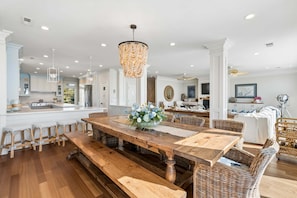 A spacious dining area with a wooden table, benches, wicker chairs, and a chandelier. - 6 BR + Bonus Room, Luxury Oceanfront, Pets ok, Elevator, 2 Living Rooms - The Loggerhead (Folly Beach)