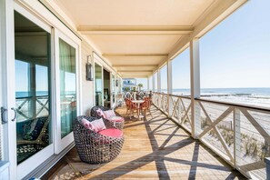 Terraza techada con mobiliario de mimbre, una mesa y sillas, con vista a la playa.