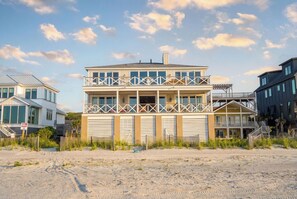 Een meerlaags gebouw aan het strand met balkon, een garage, en een zandstrand op de voorgrond.