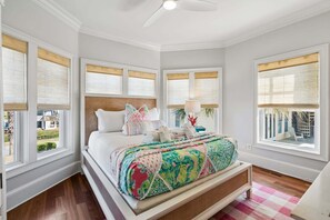 Un dormitorio con cama, ventilador de techo y ventanas amplias con persianas.