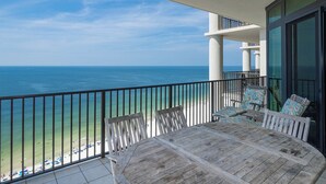 A balcony with a wooden table and chairs, overlooking a beach and the ocean. - The Oasis at Orange Beach, formerly known as Phoenix West II, Unit 2008 (Orange Beach)