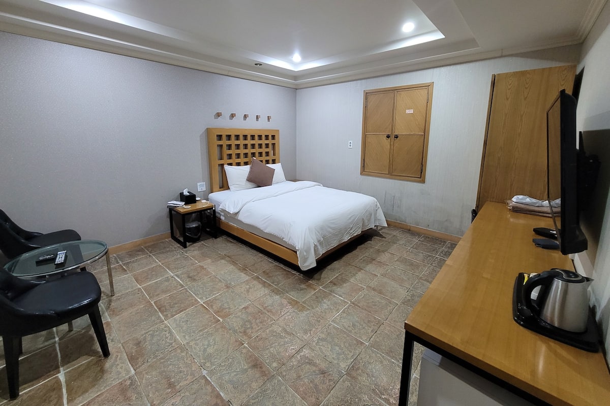 A hotel room with a bed, a desk, a chair, a television, and a wardrobe.