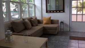 Ein Wohnzimmer mit einem beigen Sofa, einem Glastisch und einem kleinen Beistelltisch.