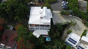 Ein mehrstöckiges Haus mit einem großen Balkon, umgeben von üppigem Grün und einem Schwimmbad.