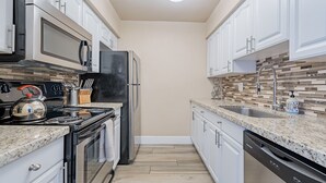 A compact kitchen with white cabinets, stainless steel appliances, a granite countertop, and a tiled backsplash.