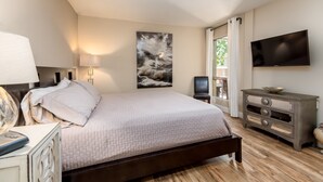A bedroom with a bed, bedside table, lamp, TV, and a painting on the wall.
