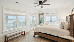 Une chambre avec un grand lit, un ventilateur de plafond et une vue sur l  ’océan grâce à de grandes fenêtres.