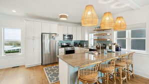 Une cuisine moderne avec des meubles blancs, des appareils en acier inoxydable et un grand îlot central doté de tabourets.