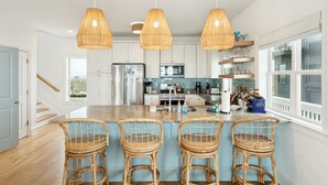 Une cuisine moderne dotée d’un îlot central, de luminaires suspendus et de tabourets de bar en osier.