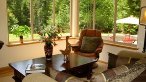 A cozy living room with a large window, a wooden coffee table, a brown leather armchair, and a beige sofa. - Beautiful, Warm & Welcoming-Redwoods, River, Beaches includes Hot tub (Arcata)