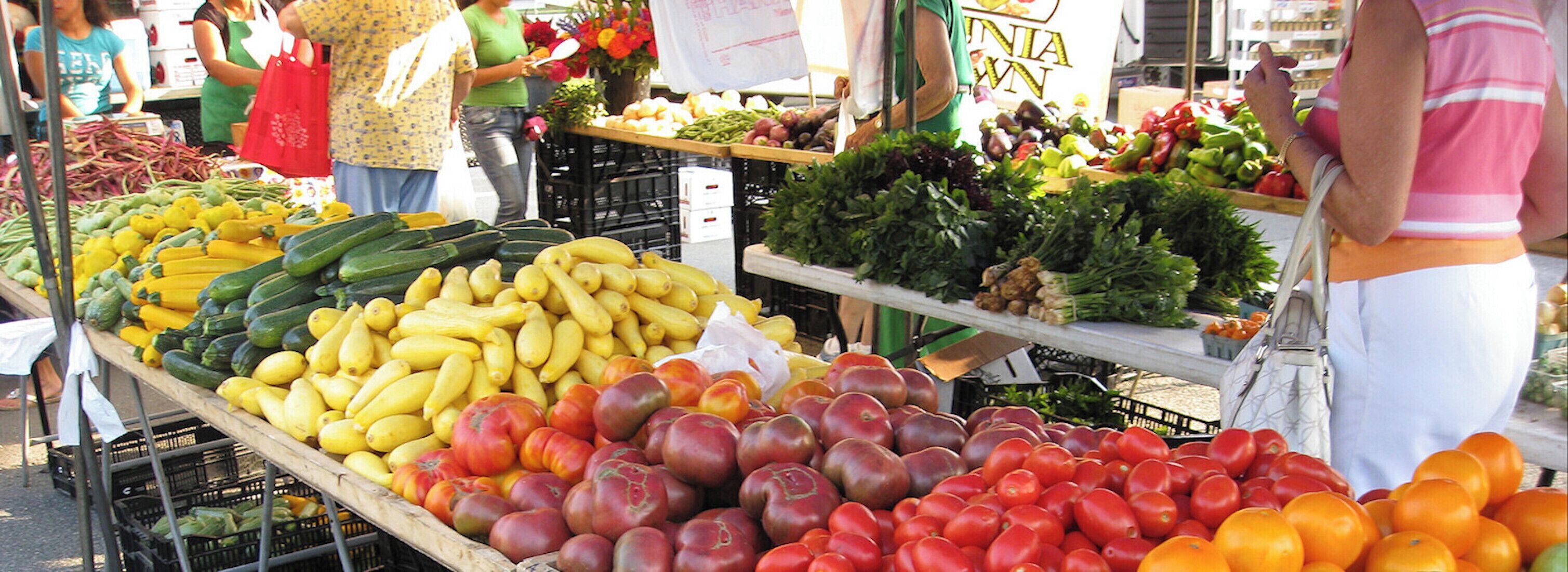 A market stall with various fruits and vegetables, including bananas, tomatoes, and leafy greens.