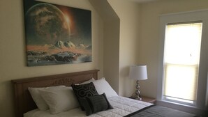 A neatly made bed with a white duvet and a dark throw blanket, a wooden headboard, a bedside lamp, and a painting of a celestial scene on the wall. - Victorian! Professionally Cleaned, Self Check In - Sleeps 10 (Kenosha)