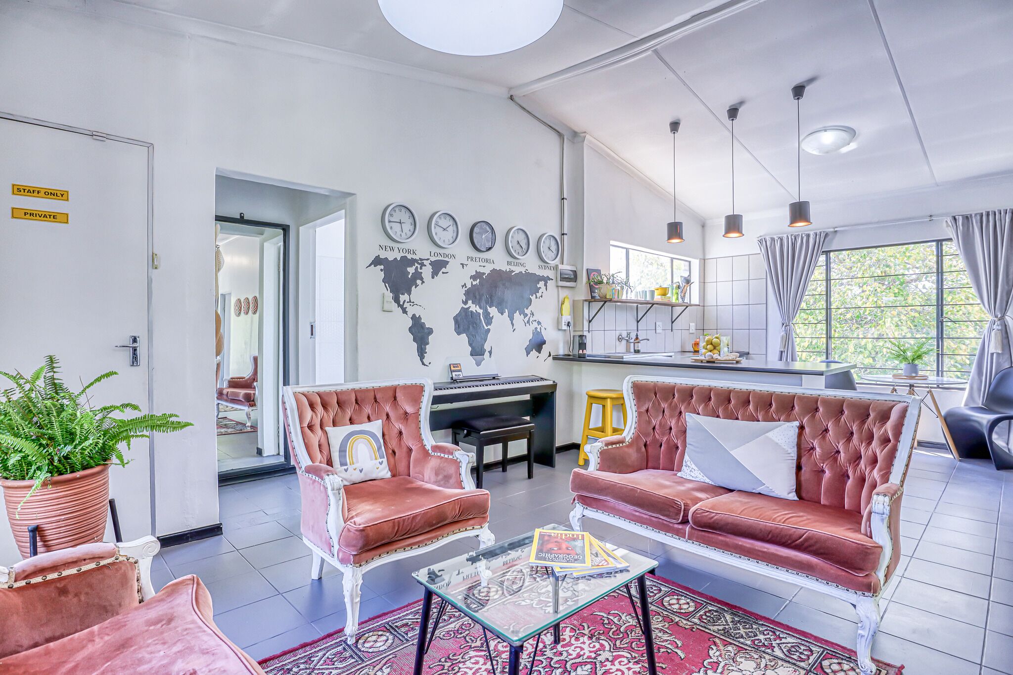 A modern hotel lobby with a seating area featuring two plush red sofas, a glass coffee table, and a world map on the wall.