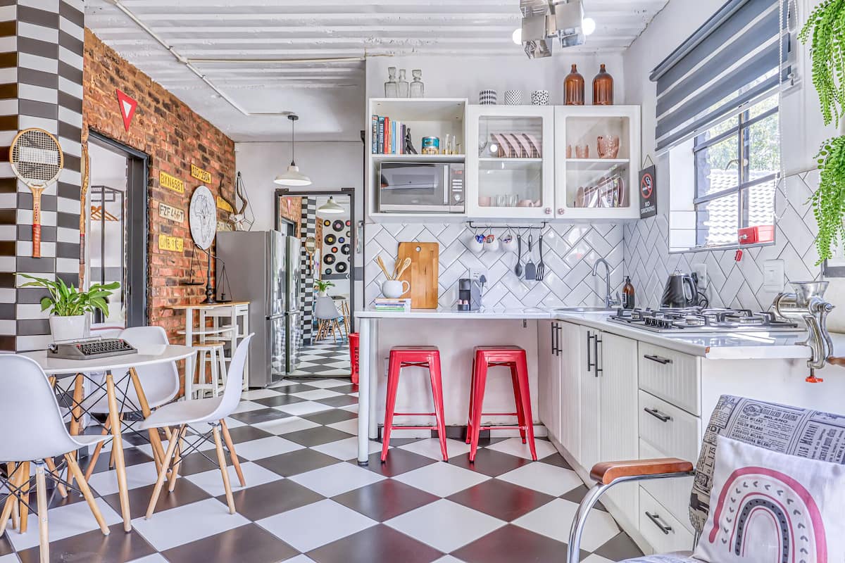 A modern kitchen with a checkered floor, white cabinets, a microwave, and red bar stools.