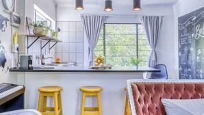 Une cuisine moderne avec un îlot central, deux tabourets jaunes, un canapé rouge à motifs et un tableau noir servant de menu, accroché au mur.