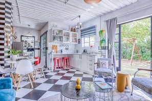Una cocina moderna con armarios blancos, piso a cuadros y un comedor con sillas blancas y sofá azul.