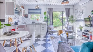 Une cuisine moderne avec des meubles blancs, un coin repas doté d’un sol à carreaux et un salon avec un canapé et une télévision.