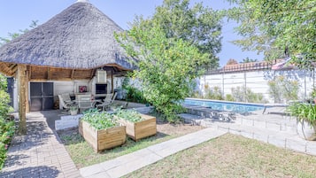 Cocina al aire libre con techo de paja, piscina y jardineras.