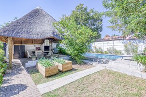 Cocina al aire libre con techo de paja, piscina y jardineras.