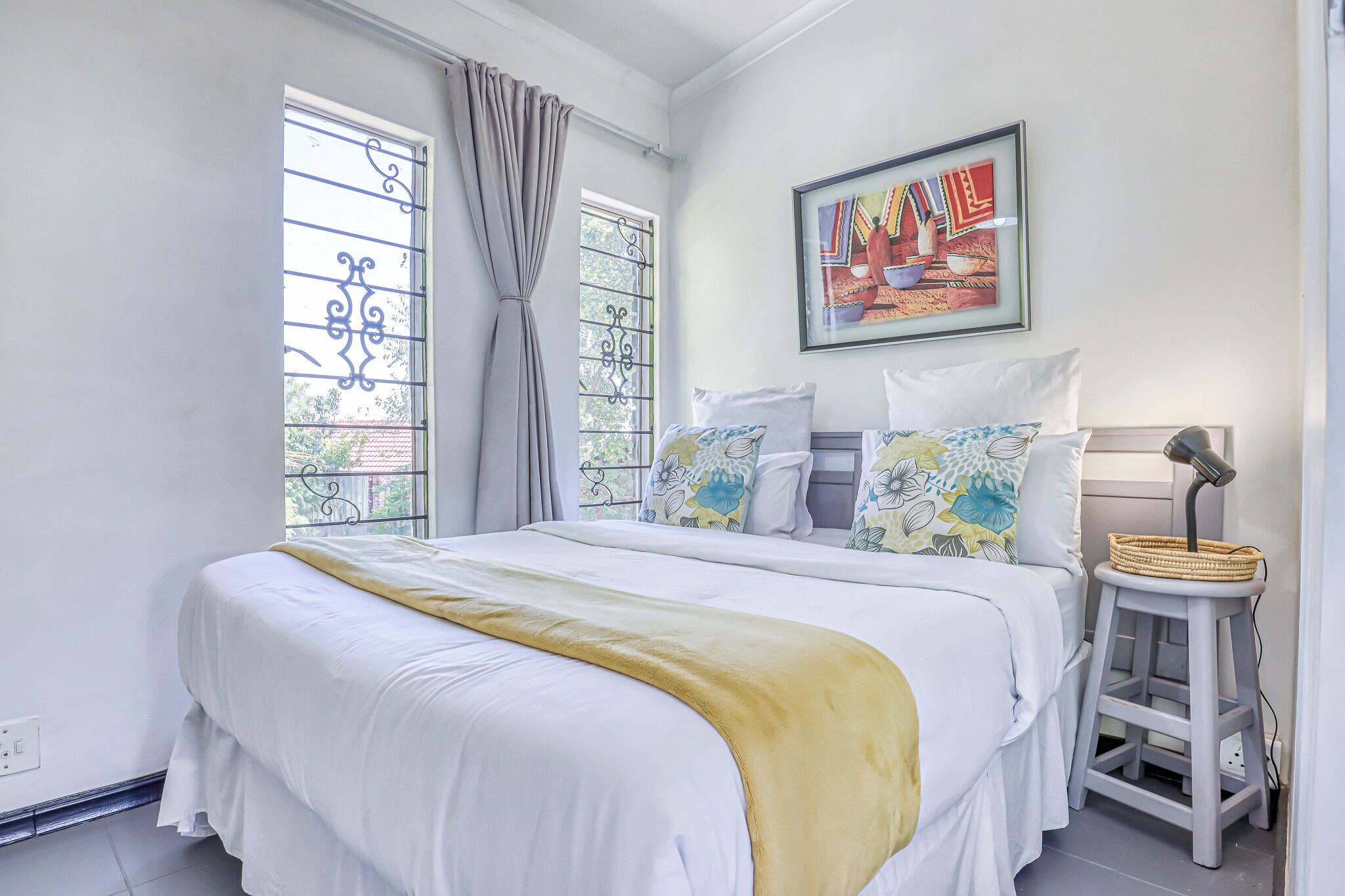 A bedroom with a large bed, a bedside table, a lamp, and a window with curtains.