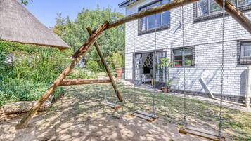 Un patio trasero con un columpio, una estructura de techo de paja y una casa de ladrillo.