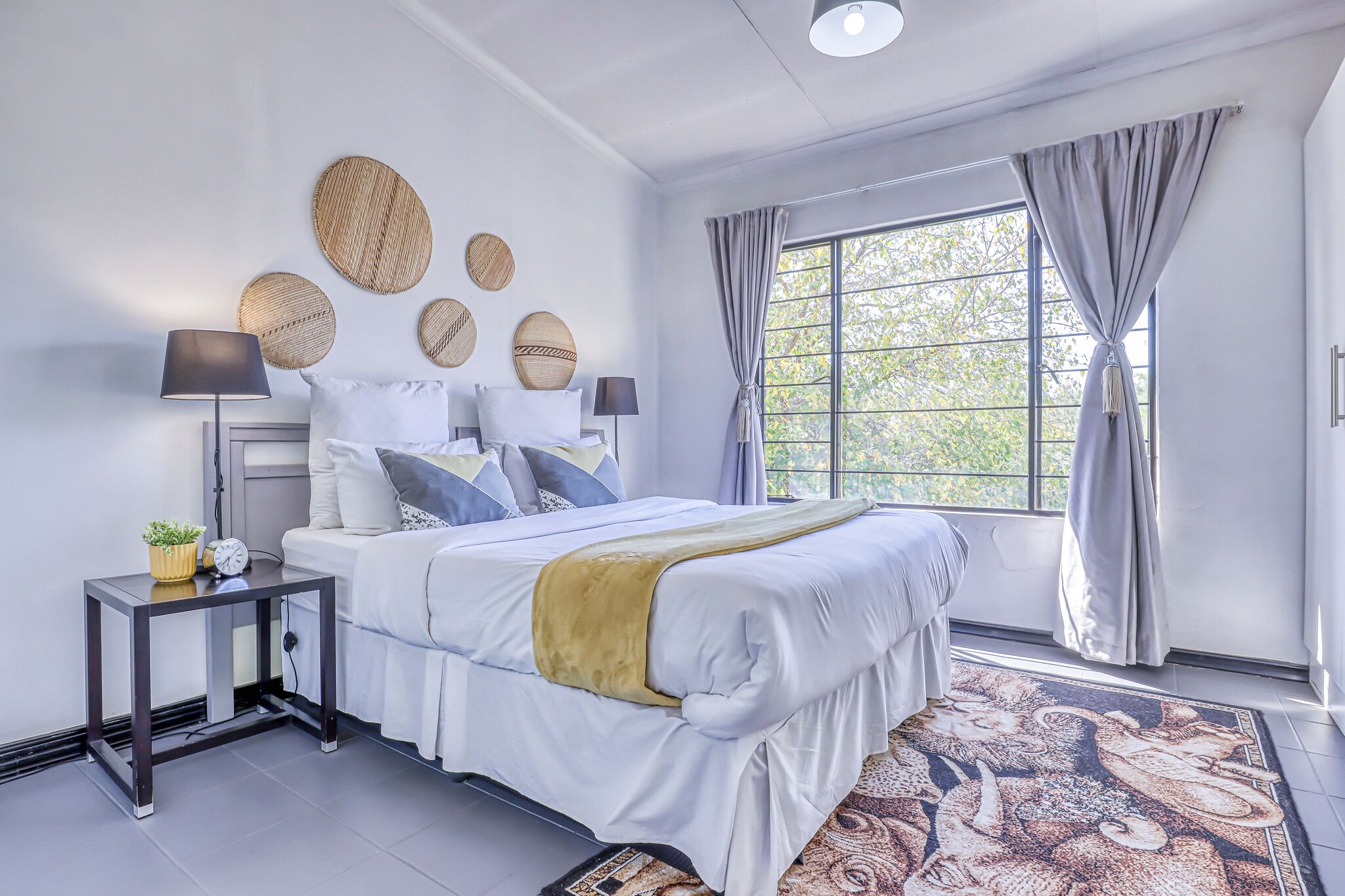A modern bedroom with a large bed, bedside tables, a window with curtains, and decorative wall art.